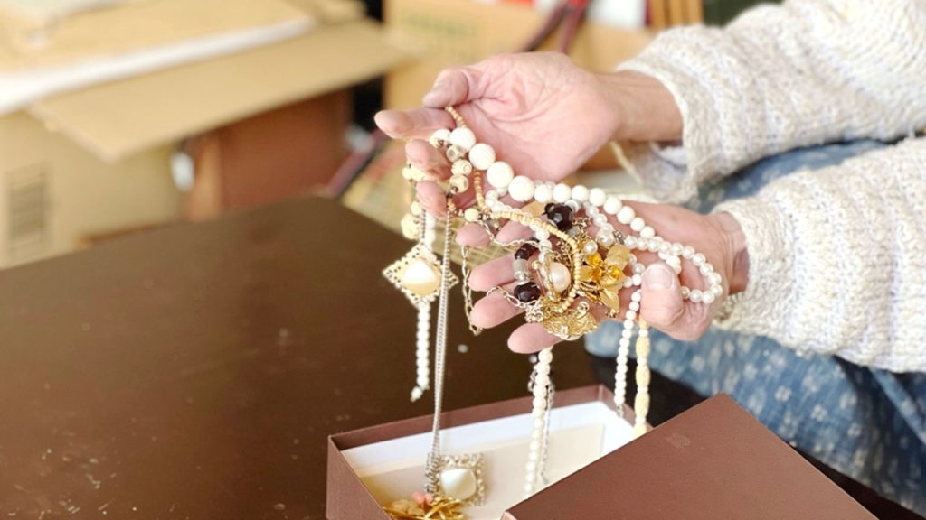 Hands holding assorted jewelry, pearl necklaces, gold and gemstone accessories, open jewelry box, vintage ornaments, elegant and intricate designs, delicate craftsmanship, personal valuables