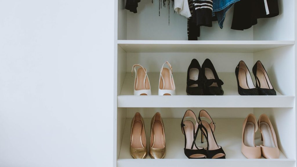 Organized closet shelves with high heels neatly arranged, hanging clothes above, white built-in wardrobe