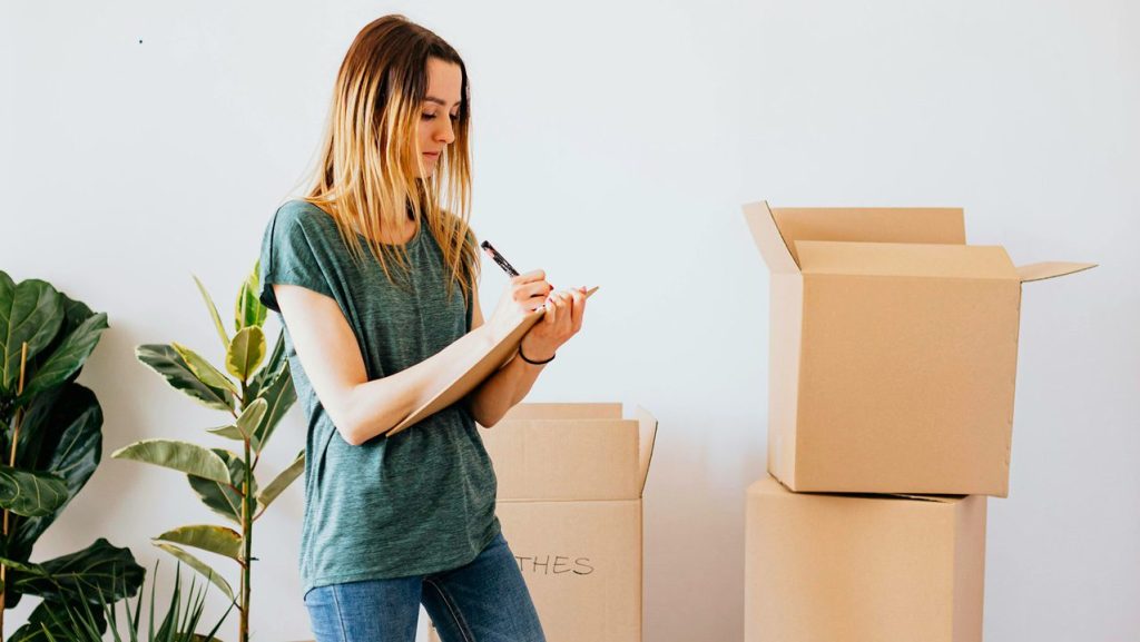 Woman writing list and organizing items in boxes while decluttering