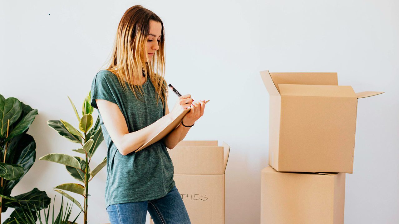 Woman writing list and organizing items in boxes while decluttering