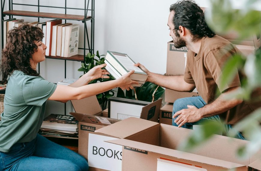 Two people packing books into cardboard boxes, organizing a home library, moving to a new place, sorting books for donation, unpacking after a move, decluttering a bookshelf