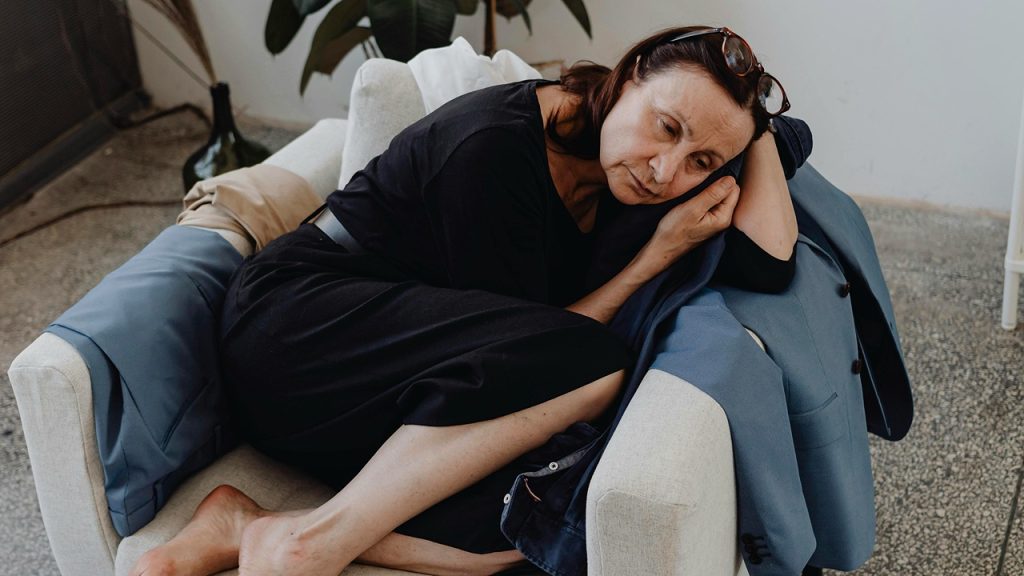 Depressed Woman, Clutter, woman in black dress curled up on couch, emotional expression, quiet indoor setting