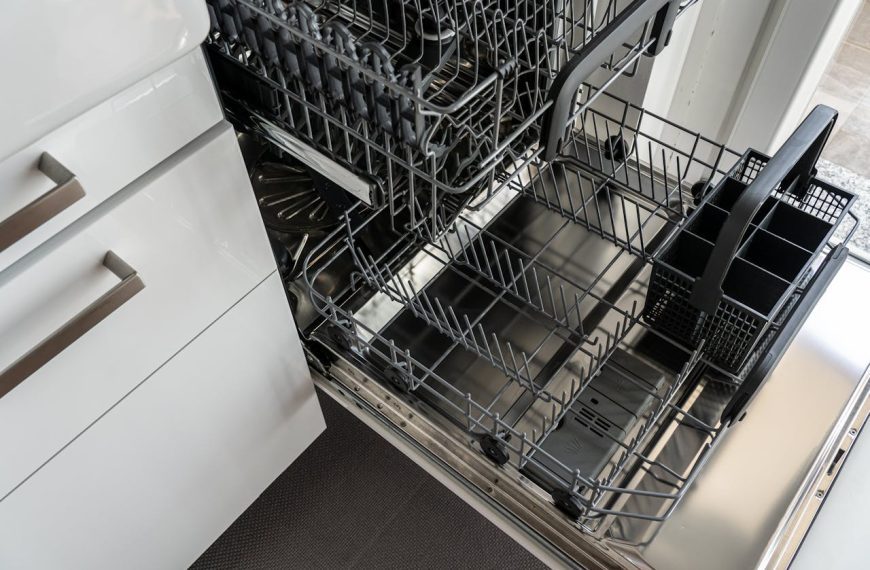Open dishwasher, empty racks extended, stainless steel interior, kitchen cabinet partially visible, ready for loading or cleaning.