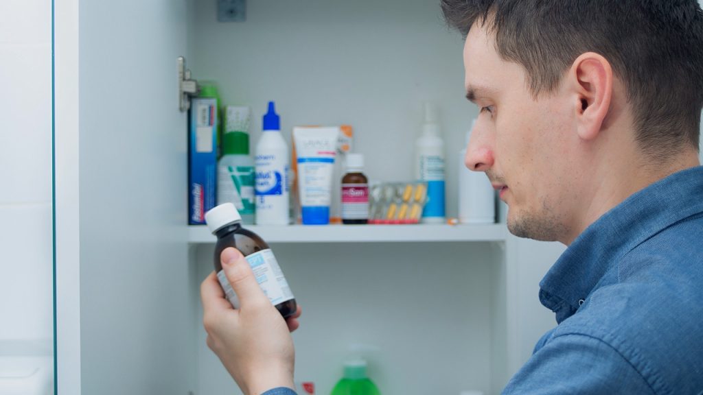 Man looking at a medicine bottle, shelves filled with various medications and health products, checking dosage or instructions