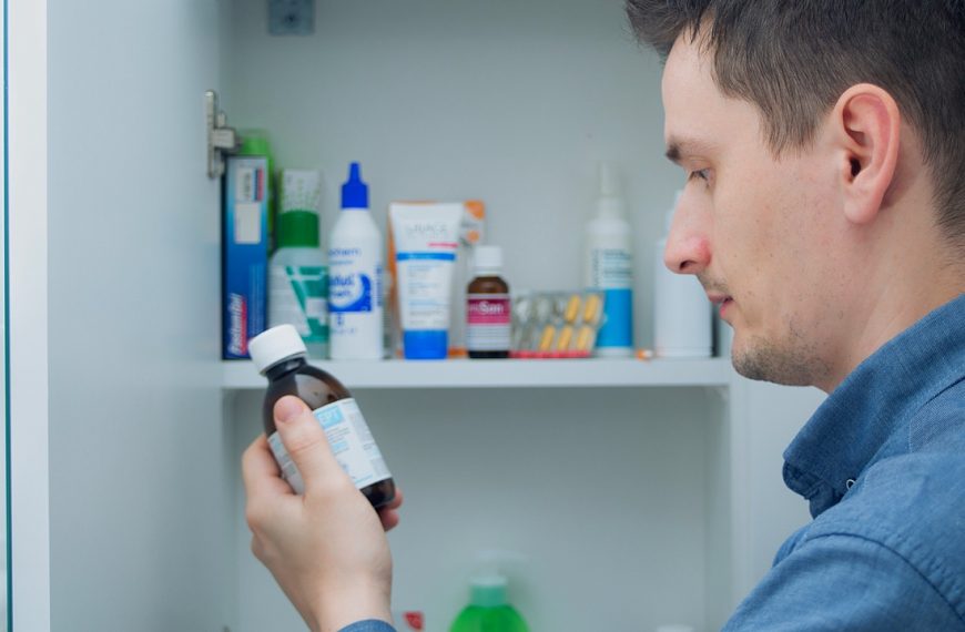 Man looking at a medicine bottle, shelves filled with various medications and health products, checking dosage or instructions