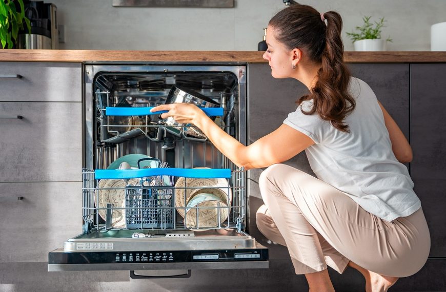Woman loading a dishwasher, placing a cup on the top rack, kitchen setting, modern appliances, cleaning dishes