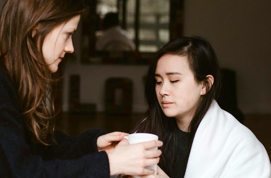 Woman handing her sick friend a cup of tea