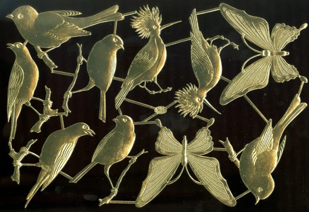 Gold embossed Dresden paper ornaments in the shapes of birds, butterflies, and branches, arranged on a dark background
