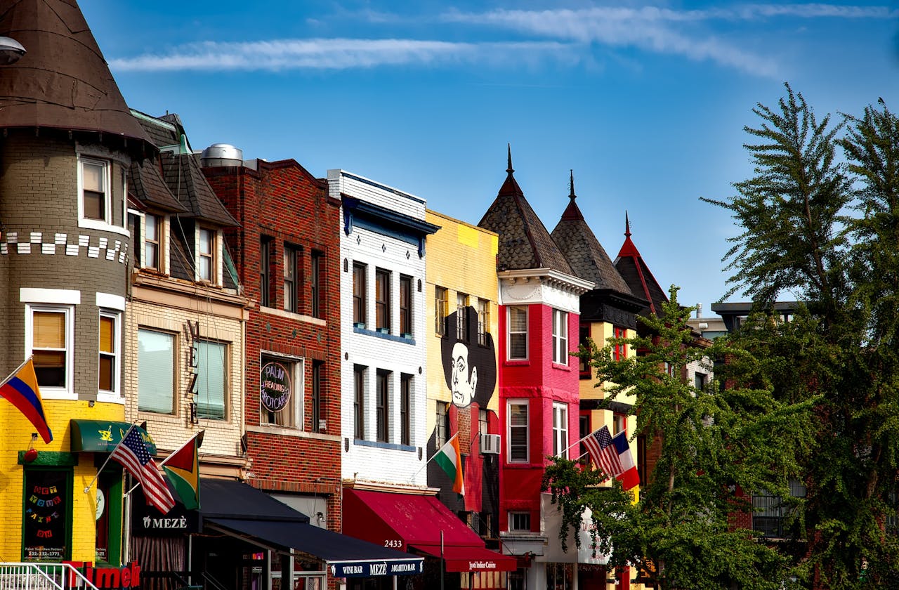 Colorful row of historic buildings, urban mural on facade, flags outside shops, clear blue sky