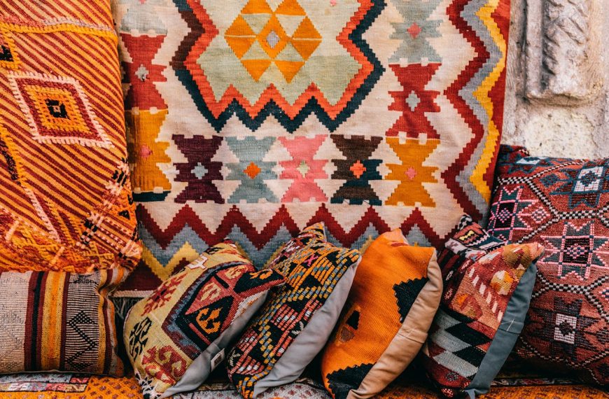 Colorful woven textile with geometric patterns, layered with patterned throw pillows, rich warm tones, traditional design