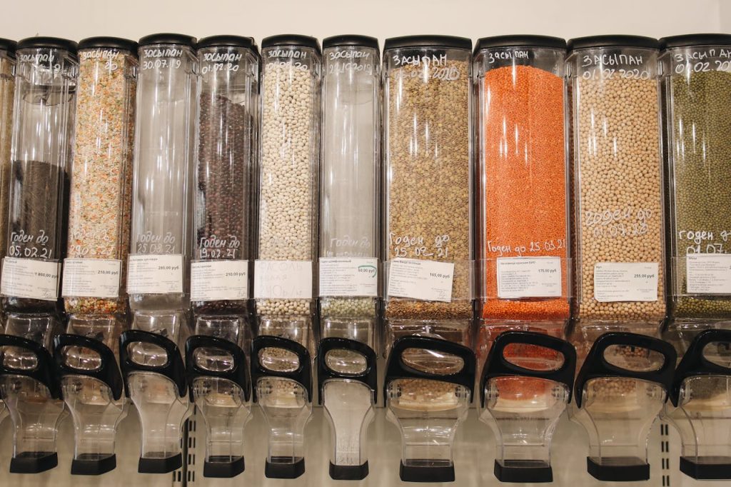 Bulk food dispensers filled with grains, legumes, and lentils, clear containers with scoops, labels and prices visible