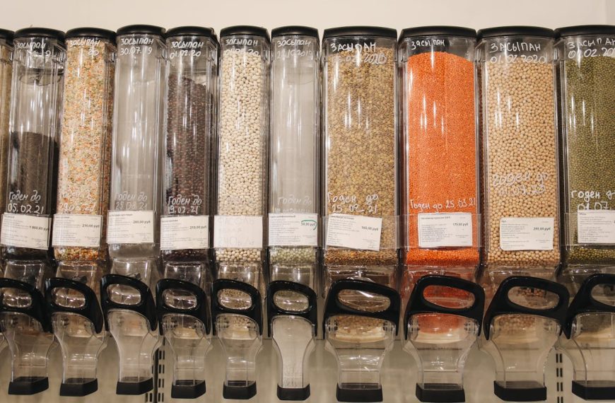 Bulk food dispensers filled with grains, legumes, and lentils, clear containers with scoops, labels and prices visible