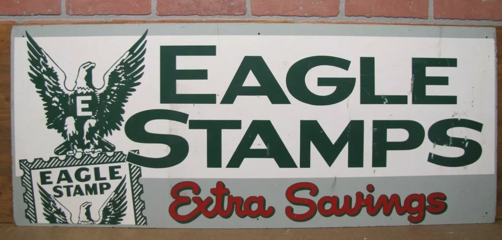 Vintage Eagle Stamps sign, green and red lettering on a white background, bold "Extra Savings" text, eagle emblem with shield, old promotional advertising