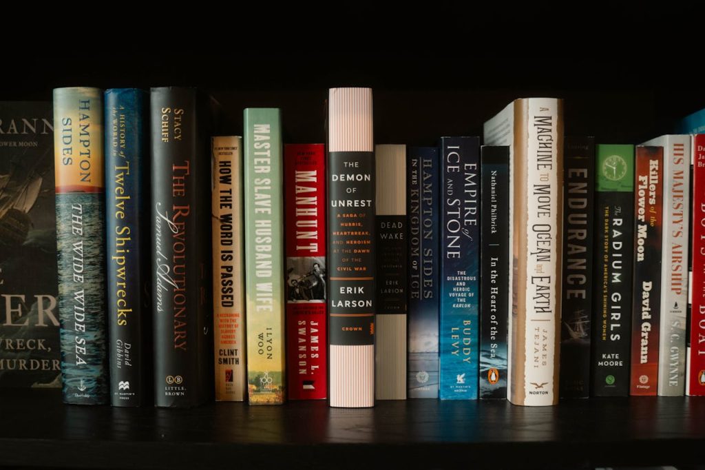 Row of assorted hardcover books on a dark shelf, spines facing outward, various genres and colors visible