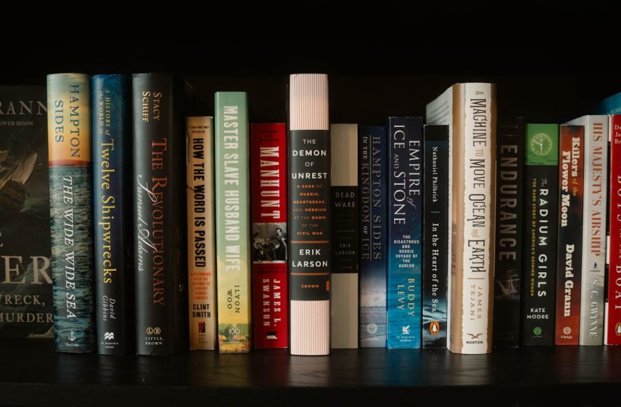 Row of assorted hardcover books on a dark shelf, spines facing outward, various genres and colors visible