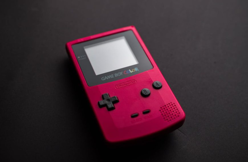 A red Nintendo Game Boy Color handheld console placed on a dark surface, with visible buttons, screen, and logo