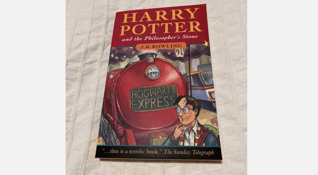 Cover of “Harry Potter and the Philosopher’s Stone” by J.K. Rowling, red Hogwarts Express train, Harry in glasses, bold title on maroon background