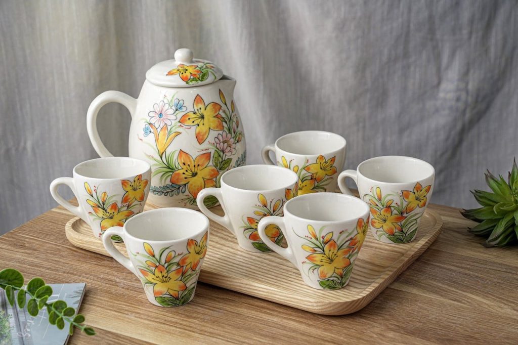 Floral tea set with teapot and six matching cups, yellow flower design, placed on wooden tray, light background