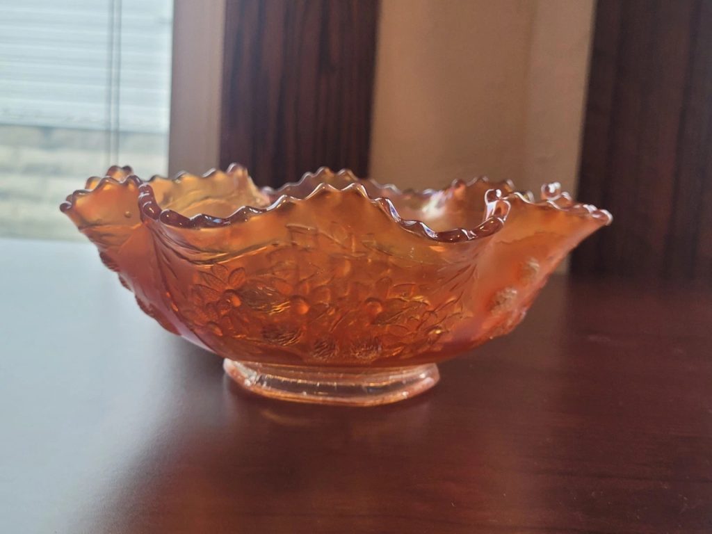 Decorative orange glass bowl, ruffled edge design, textured surface with bubble-like patterns, placed on a polished wooden table