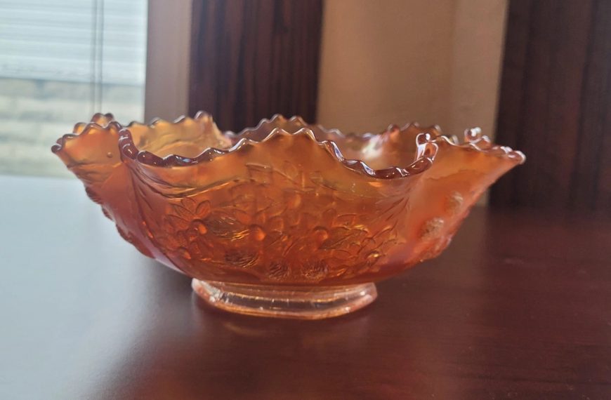 Decorative orange glass bowl, ruffled edge design, textured surface with bubble-like patterns, placed on a polished wooden table