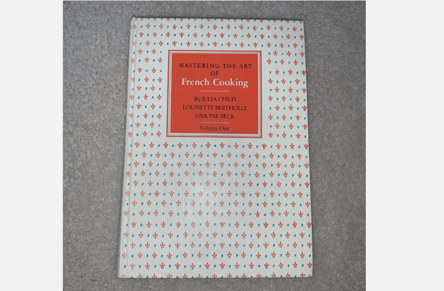 Mastering the Art of French Cooking book, Volume One, patterned white and red cover, laying on gray surface