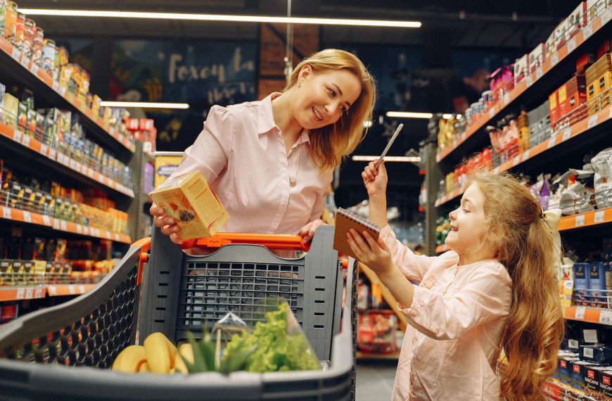 Woman and young girl grocery shopping, standing beside a cart, smiling, checking items on a shopping list