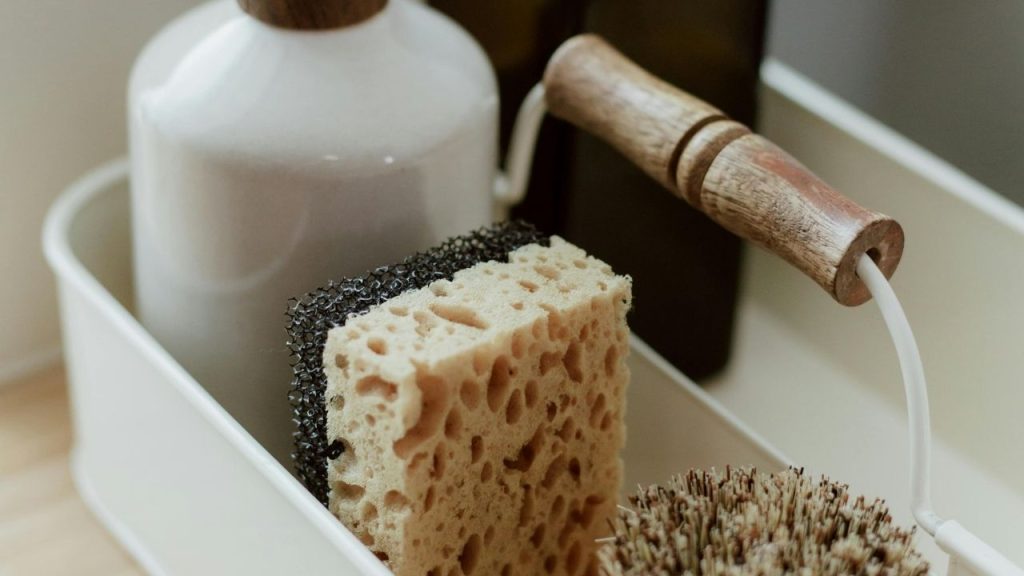 Close-up of a cleaning caddy, natural sponge, scrub brush with a wooden handle, dish soap bottle, kitchen cleaning tools