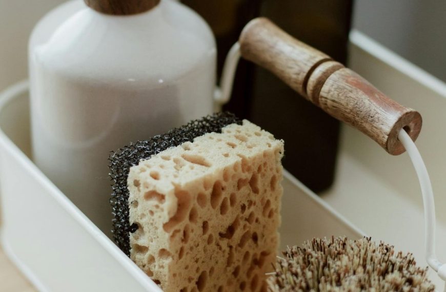 Close-up of a cleaning caddy, natural sponge, scrub brush with a wooden handle, dish soap bottle, kitchen cleaning tools