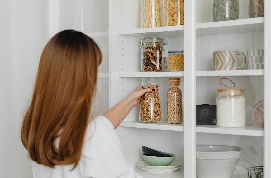 Woman arranging jars on pantry shelves for organized food storage.