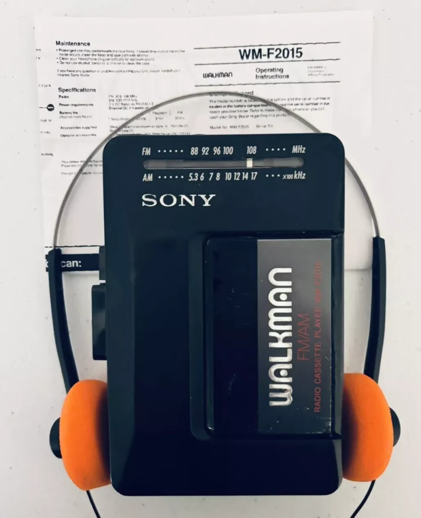 Sony Walkman cassette player, black design with silver lettering, paired with retro orange foam headphones, classic portable music device, vintage audio technology