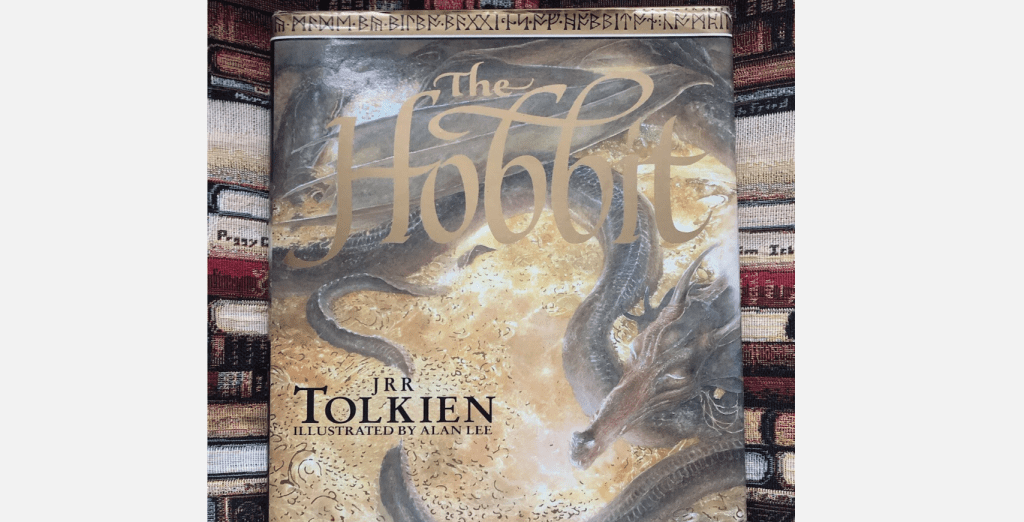 Book cover of The Hobbit, gold and brown tones, title in large decorative font, illustrated dragon wrapping around gold treasure, author J.R.R. Tolkien credited