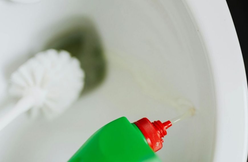 Green bottle with red nozzle, liquid cleaner being poured, toilet cleaning in progress disinfecting bathroom surfaces, household cleaning product, removing stains and germs, close-up of cleaning process