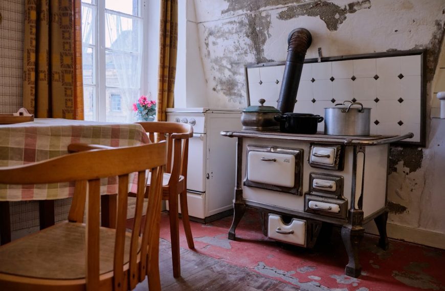 Old-fashioned kitchen with vintage stove, pots on top, wooden chairs, floral tablecloth, soft natural light