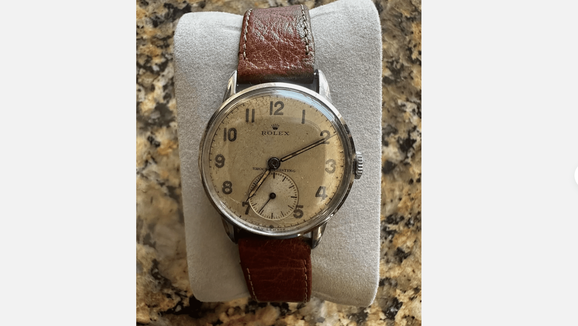 Vintage Bulova wristwatch, cream dial, silver casing, brown leather strap, displayed on a white cushion, granite background