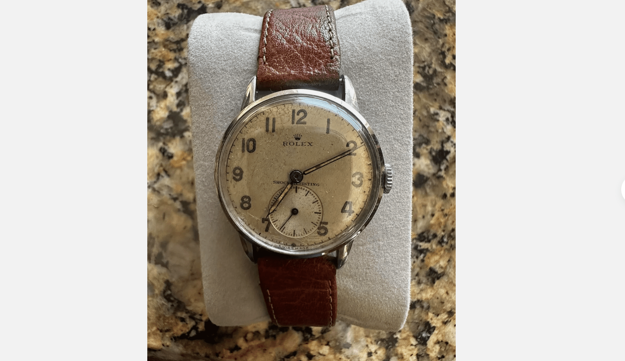 Vintage Bulova wristwatch, cream dial, silver casing, brown leather strap, displayed on a white cushion, granite background