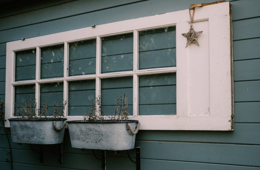 Old window with white frame on blue wooden wall, two metal planters with dried plants, hanging star decoration