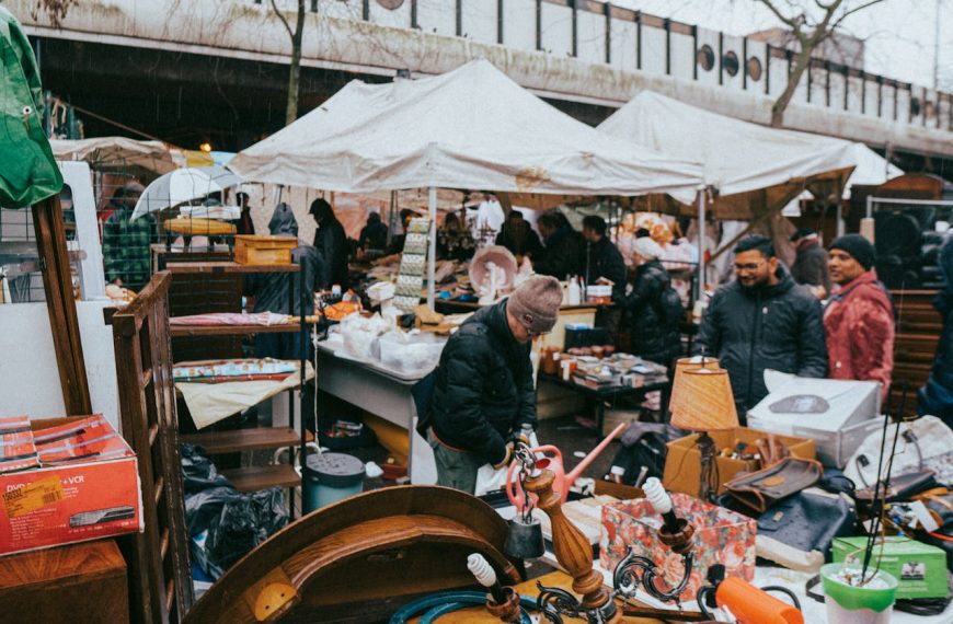 crowded flea market scene, shoppers browsing stalls, vintage items on tables, white tents, cool weather clothing