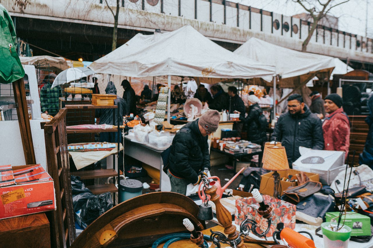 crowded flea market scene, shoppers browsing stalls, vintage items on tables, white tents, cool weather clothing