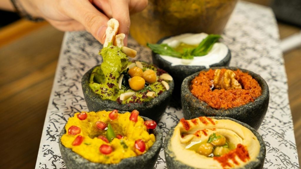 bowls of hummus surrounded by colorful veggie sticks