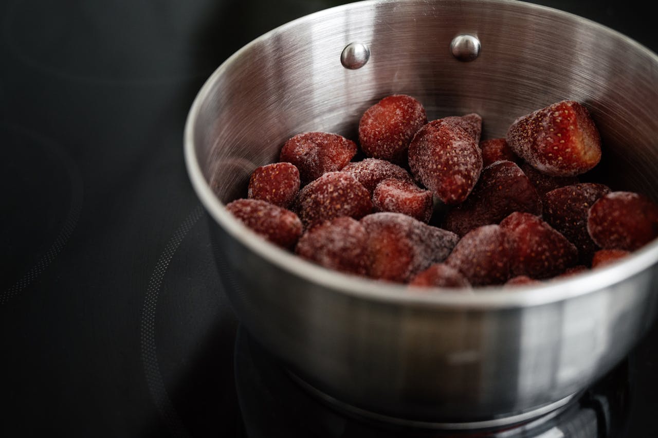 Frozen strawberries in a stainless steel pot, placed on a black stovetop, ready for cooking or defrosting