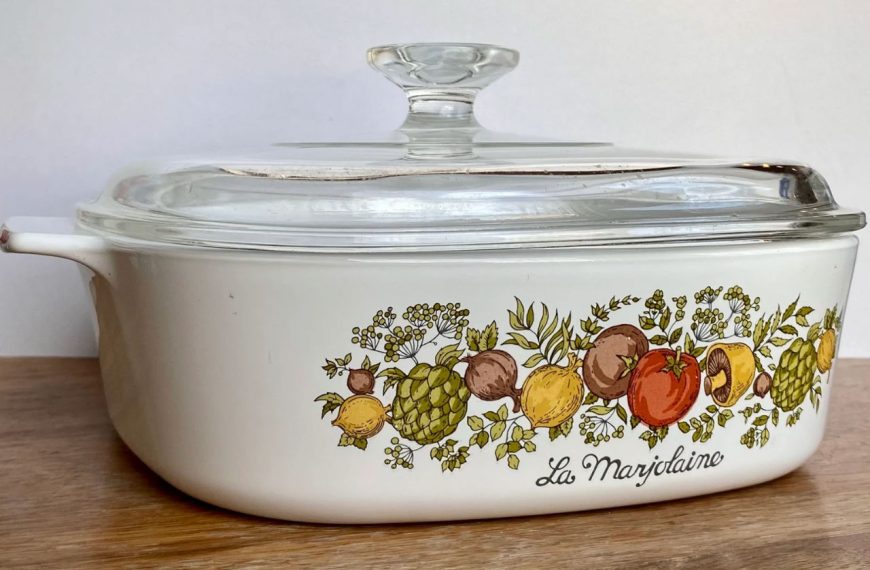 White vintage casserole dish, glass lid, vegetable-themed floral pattern on side, wooden surface background, labeled “La Marjolaine