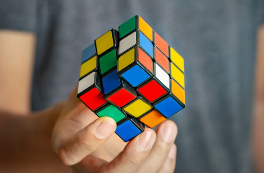 Hand holding a partially scrambled Rubik’s Cube with colorful tiles against a blurry background