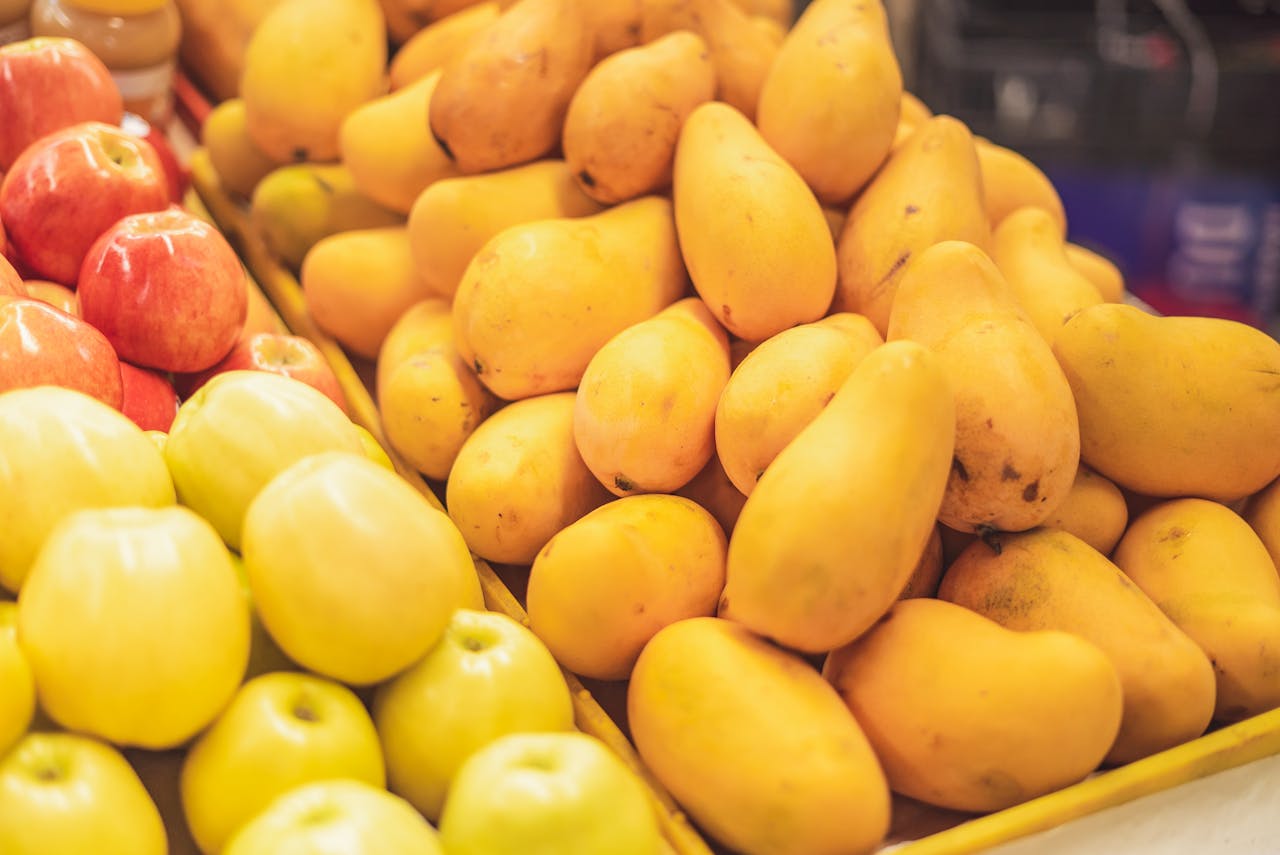 Close-up of fresh mangoes, red apples, and yellow apples displayed on market stall, bright and colorful fruit arrangement