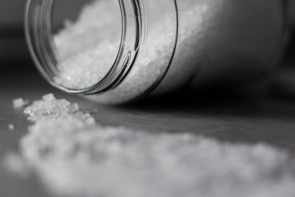 Spilled glass jar, fine white powder scattered on a surface, close-up, black and white image, soft focus on foreground