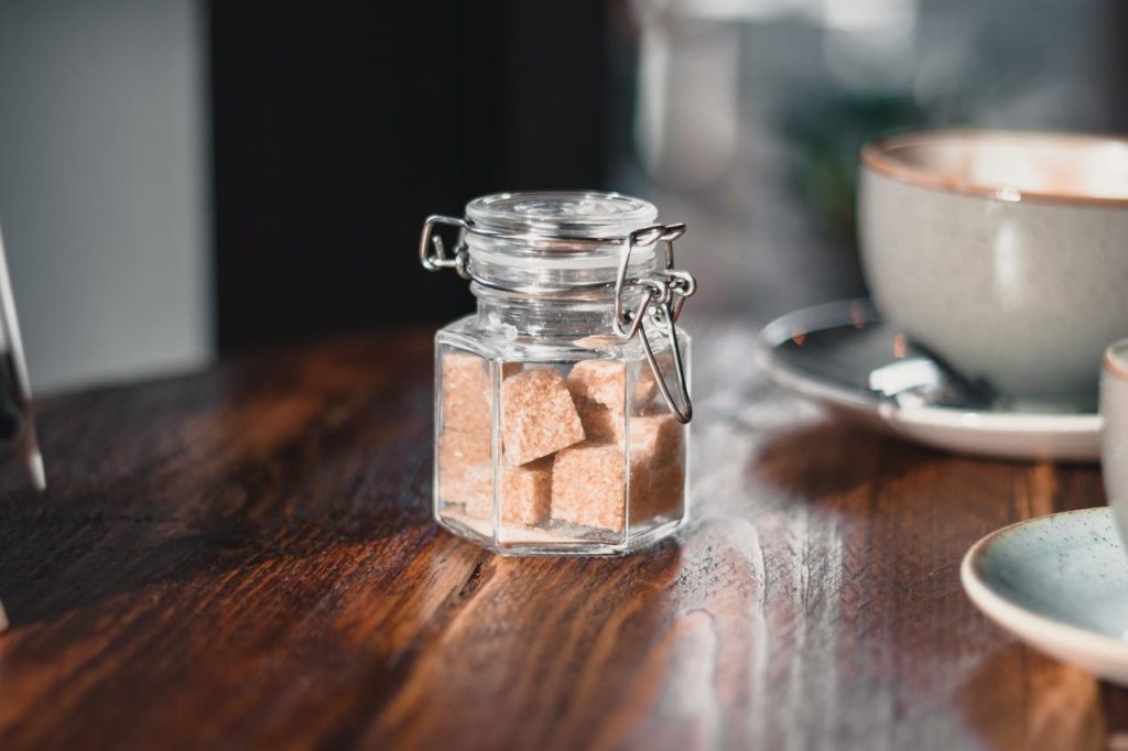 glass jar with latch lid, filled with brown sugar cubes, placed on wooden table, soft natural light in background