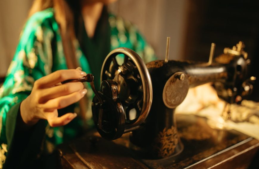 Close-up of a vintage sewing machine, woman's hand adjusting the wheel, warm lighting, blurred background, focused on sewing work, nostalgic atmosphere