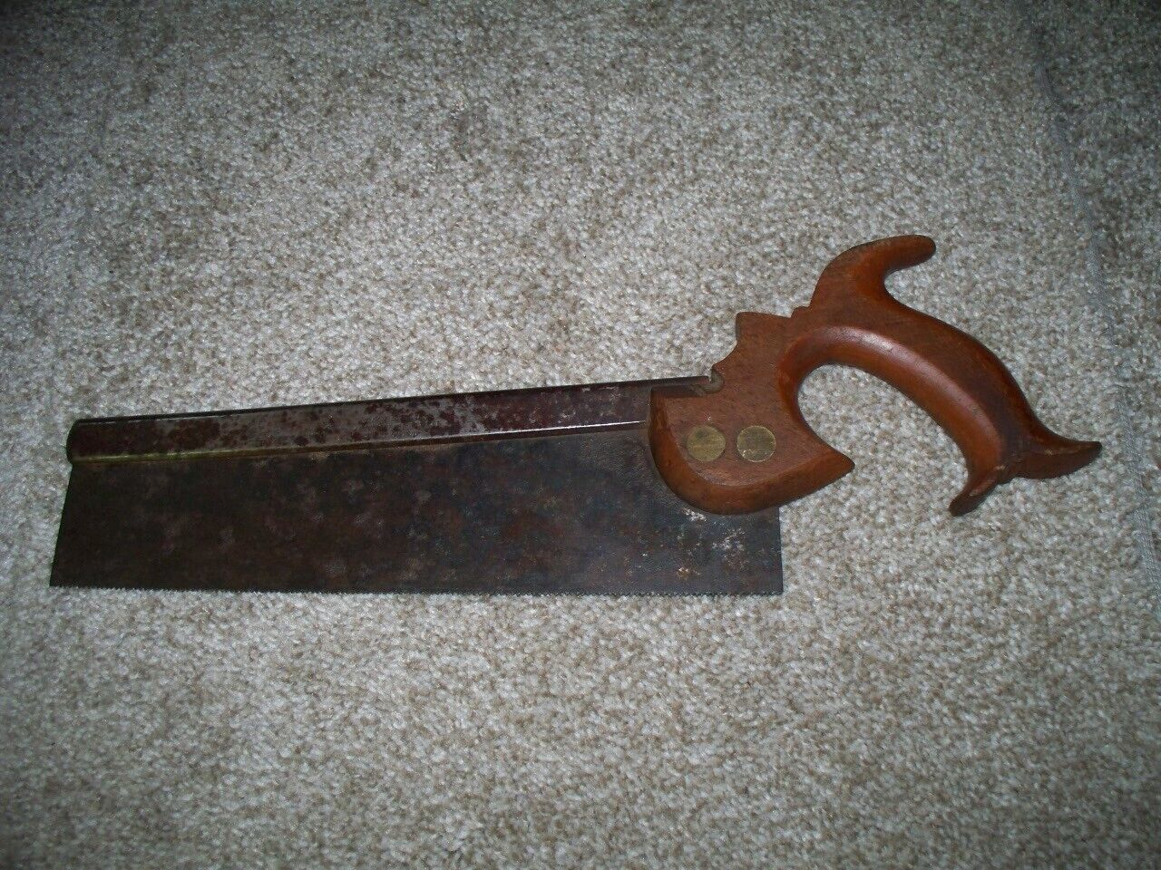 Vintage back saw with a dark wooden blade and a curved wooden handle, resting on a light-colored carpeted surface
