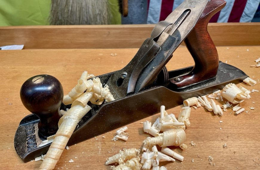 Wooden hand plane on a workbench, surrounded by wood shavings, metal blade visible, dark wooden handle, used for smoothing wood surfaces, traditional woodworking tool
