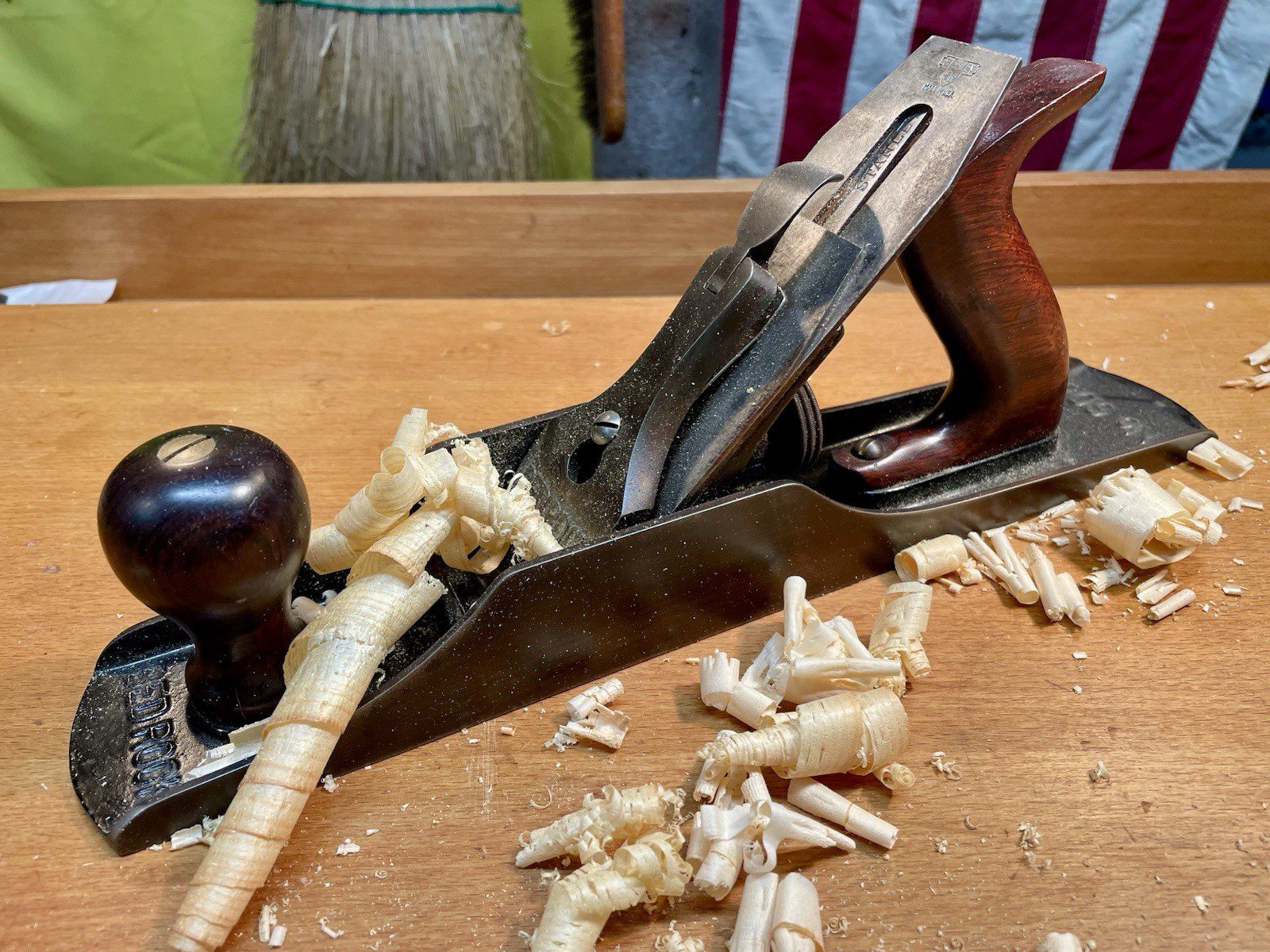 Wooden hand plane on a workbench, surrounded by wood shavings, metal blade visible, dark wooden handle, used for smoothing wood surfaces, traditional woodworking tool