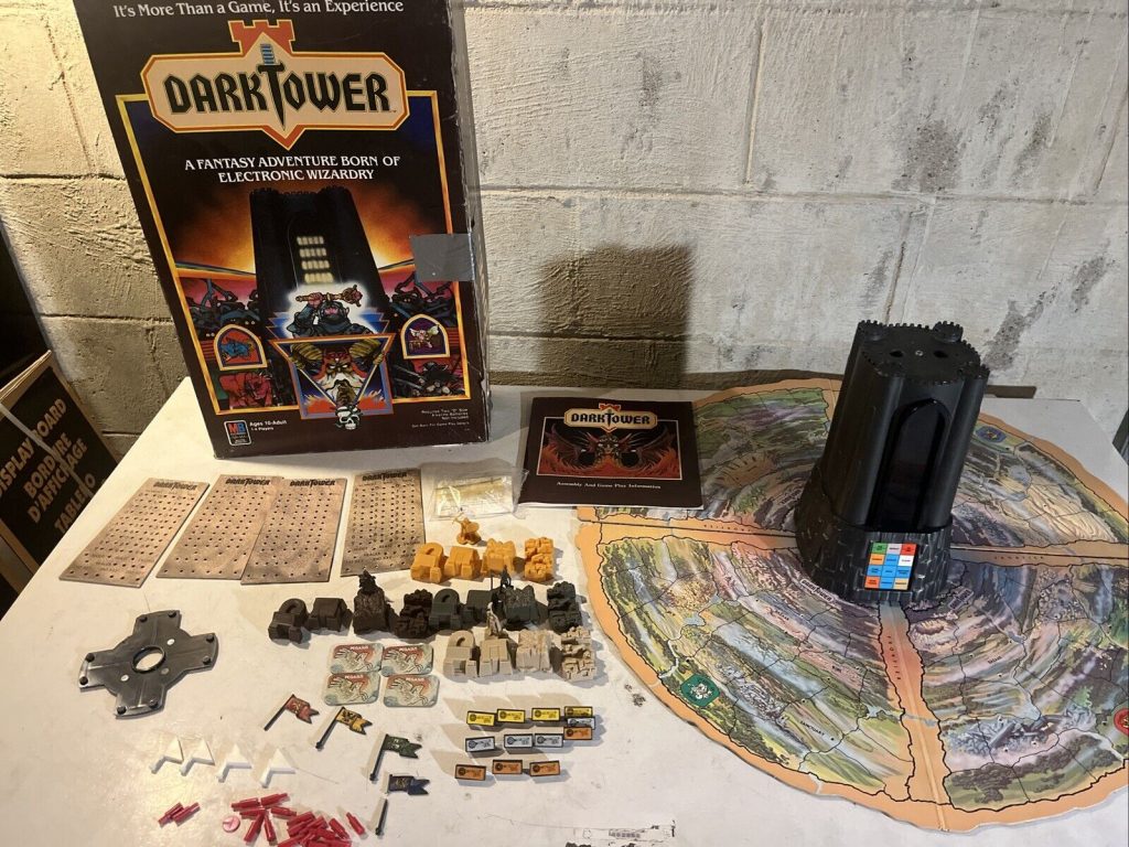 Vintage Dark Tower board game with box, electronic tower, map, game pieces, and cards spread out on a table, against a concrete wall background